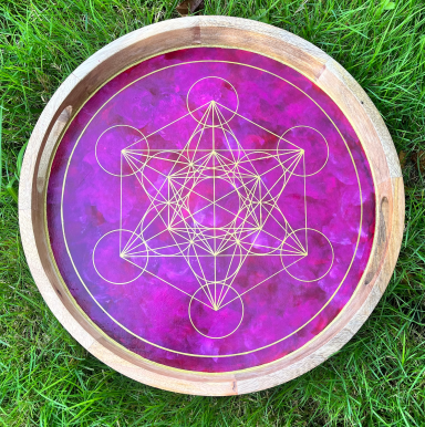 Mandala géométrique doré sur fond rose, disposé dans un plateau en bois.
